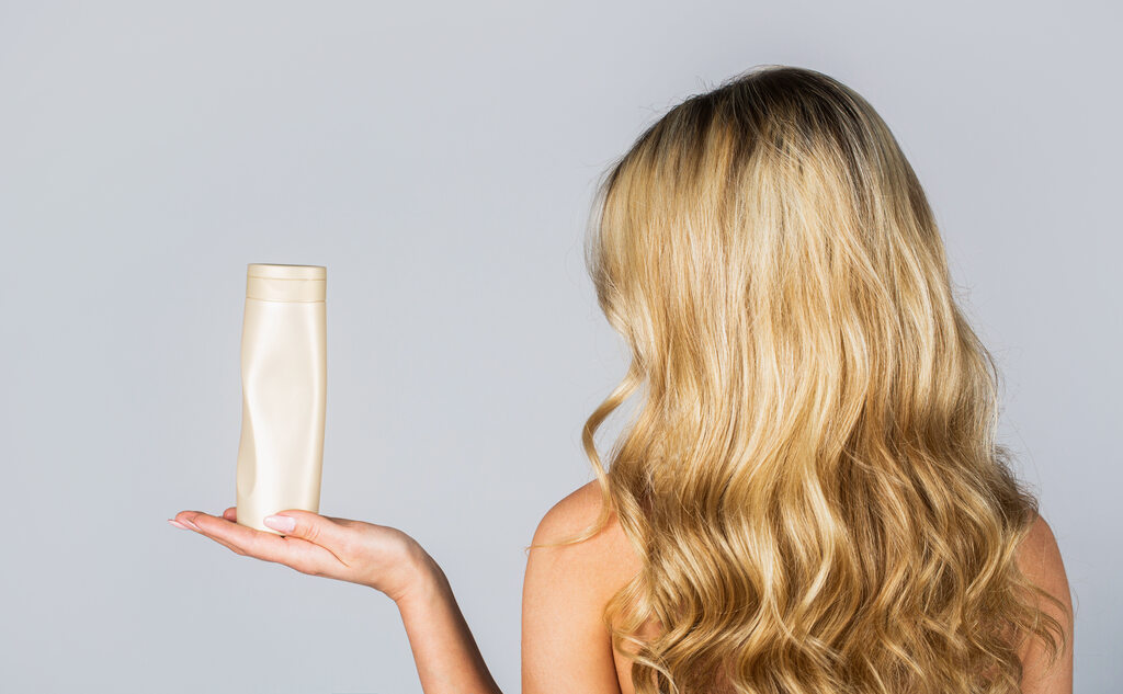 mulher com cabelo loiro sedoso utilizando silicone para cosméticos em composição do seu shampoo
